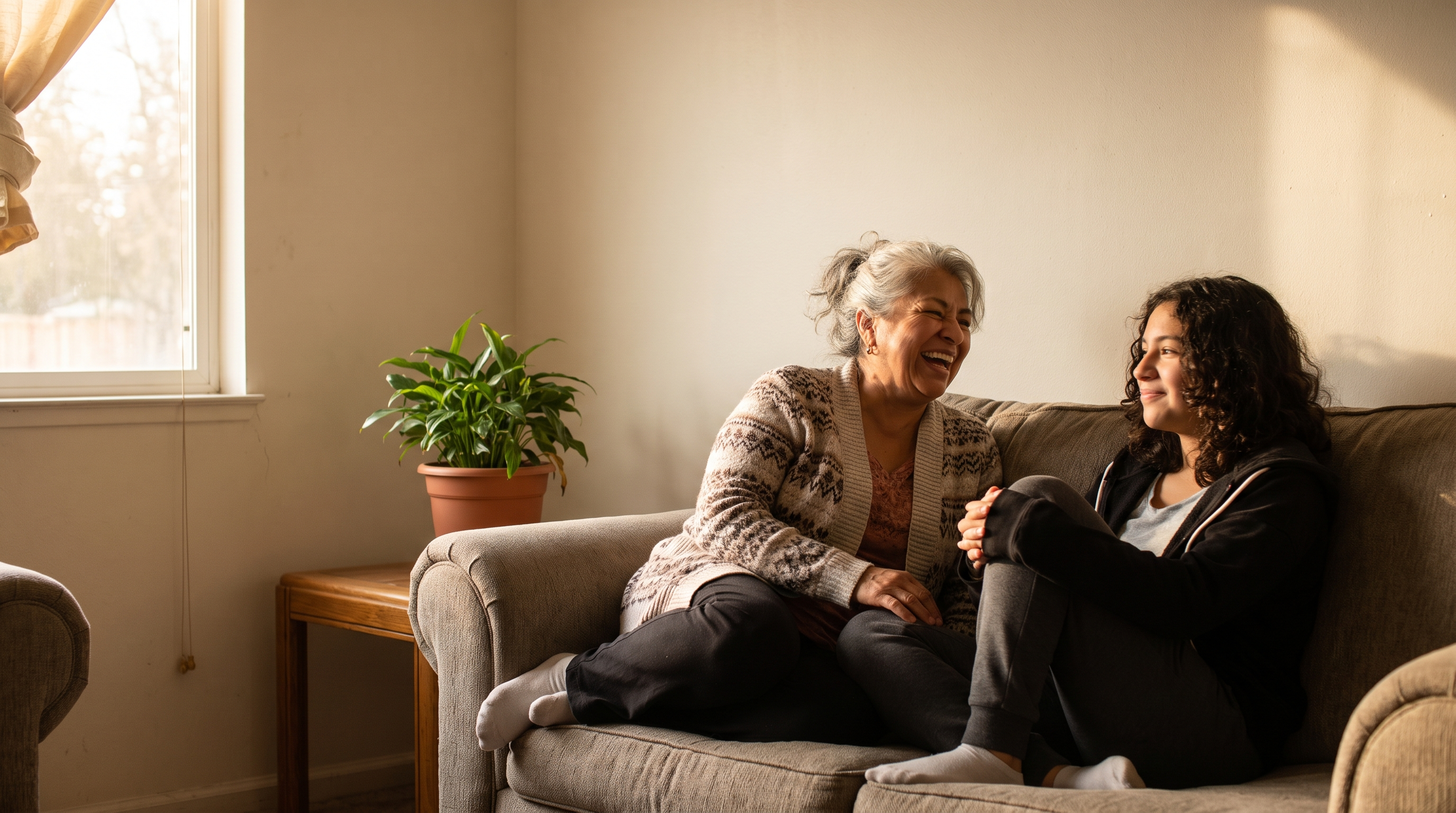 A grandmother in her 70s laughs with her granddaughter on the sofa