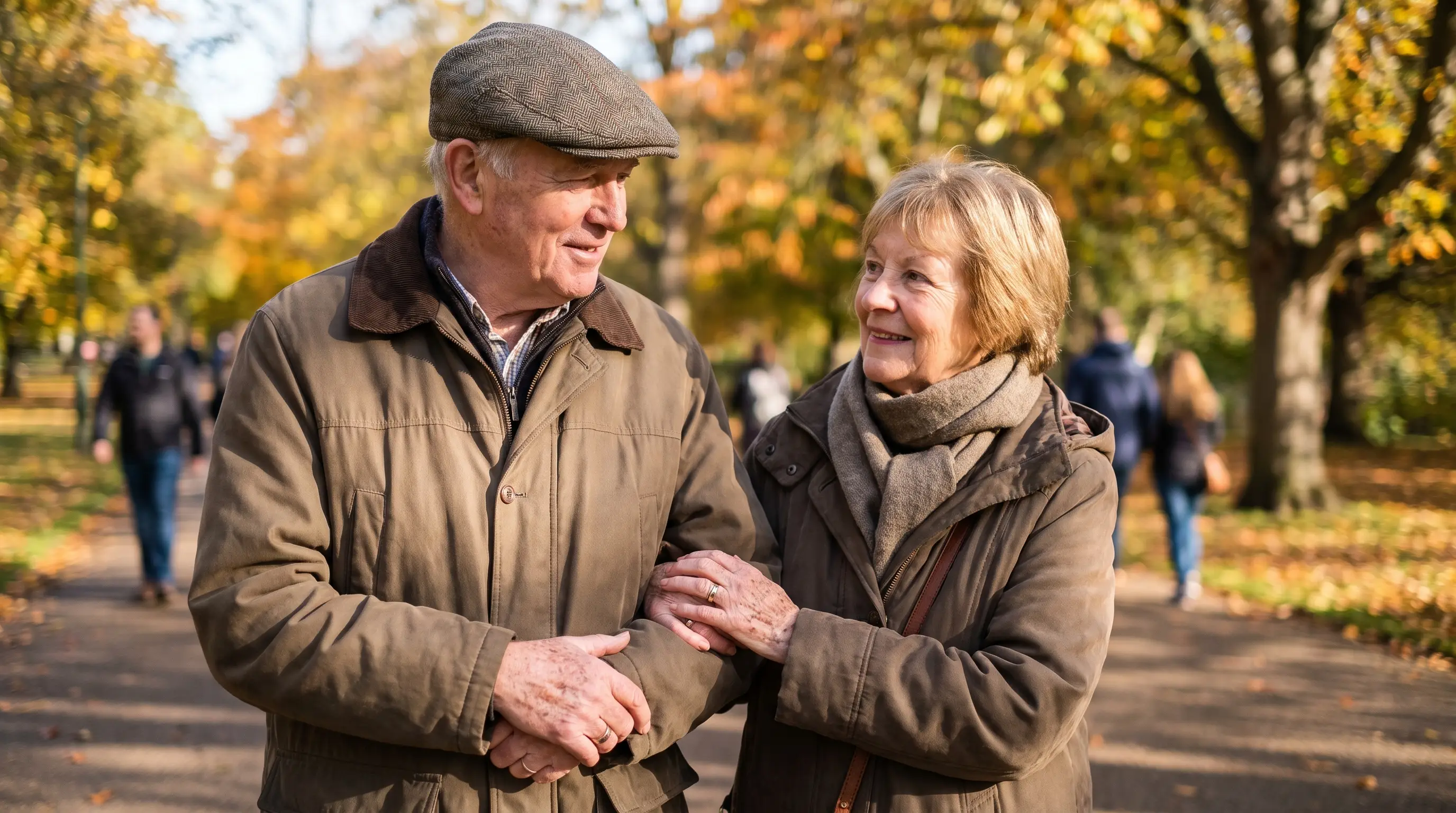 A couple in their 70s walk arm in arm on a park path in autumn